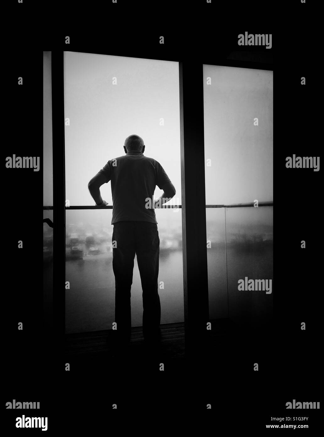 Male figure gripping a balcony rail overlooking a river - Smartphone Captured Stock Image