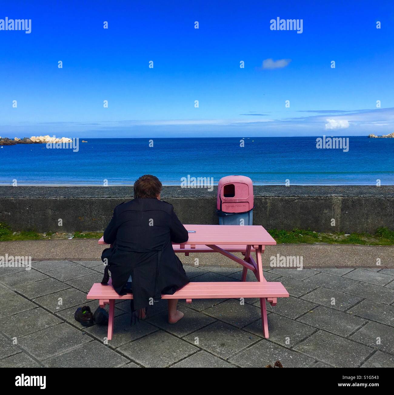 A man sitting on the pink bench in the beach in Guernsey Stock Photo