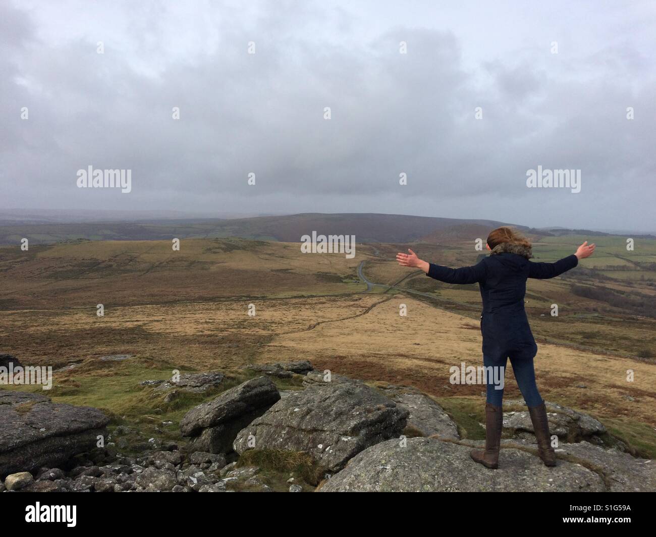 A woman stands atop a tor looking out at Dartmoor in the UK Stock Photo
