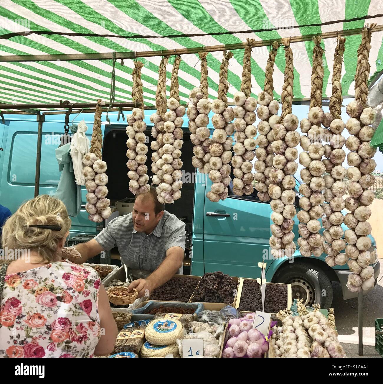 A woman buys garlic from a market trader in Nerja, Andalusia, Spain. - Smartphone Captured Stock Image