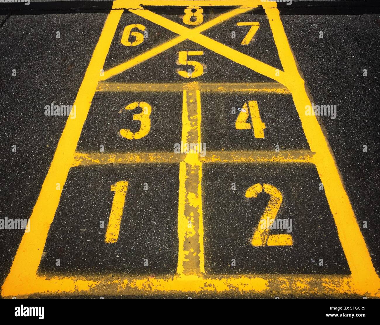 Numbers one through eight painted in yellow on a hopscotch game board on cement - Smartphone Captured Stock Image