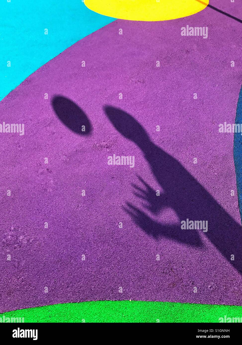 The shadow of a child who is throwing a ball into the air and trying to catch it. The background is the colourful soft flooring of a playground. An image with multiple uses. Photo © COLIN HOSKINS. - Smartphone Captured Stock Image