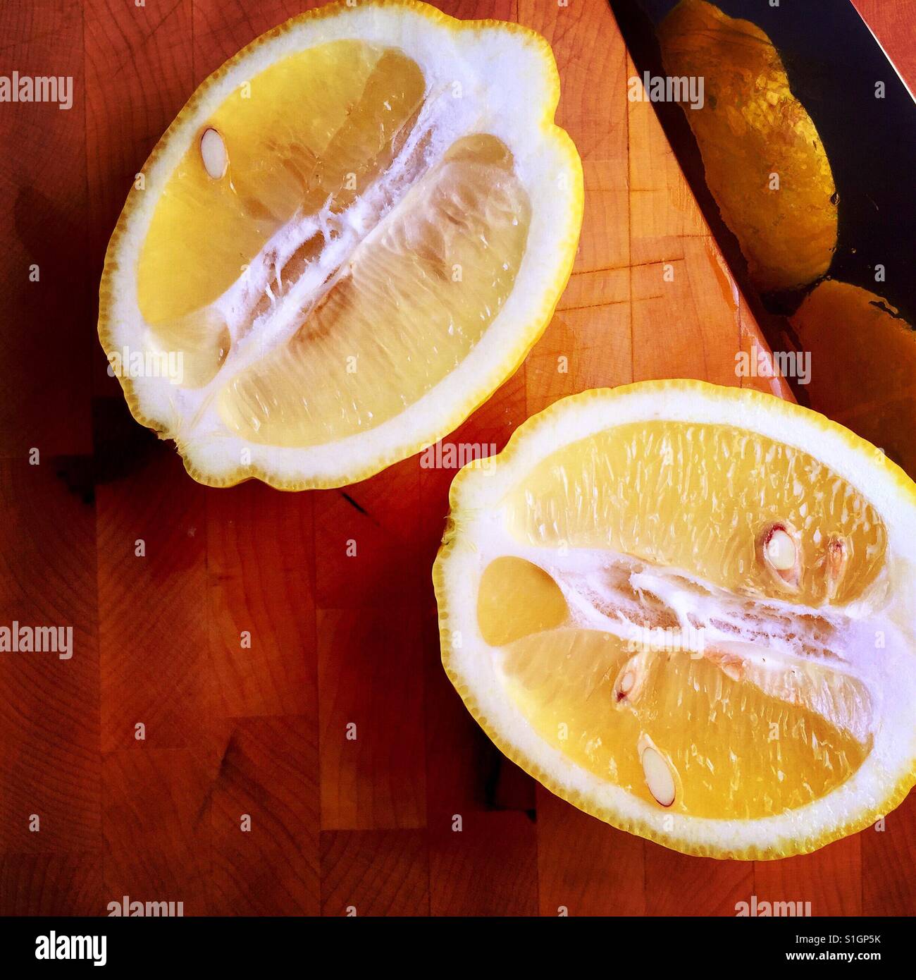 A fresh lemon cut in half on a wood cutting board with a knife Stock Photo