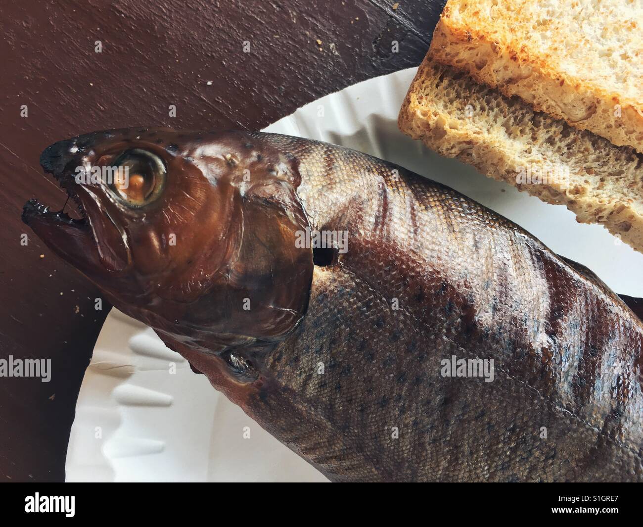 Smoked trout on a disposable paper plate with two slices of bread Stock Photo