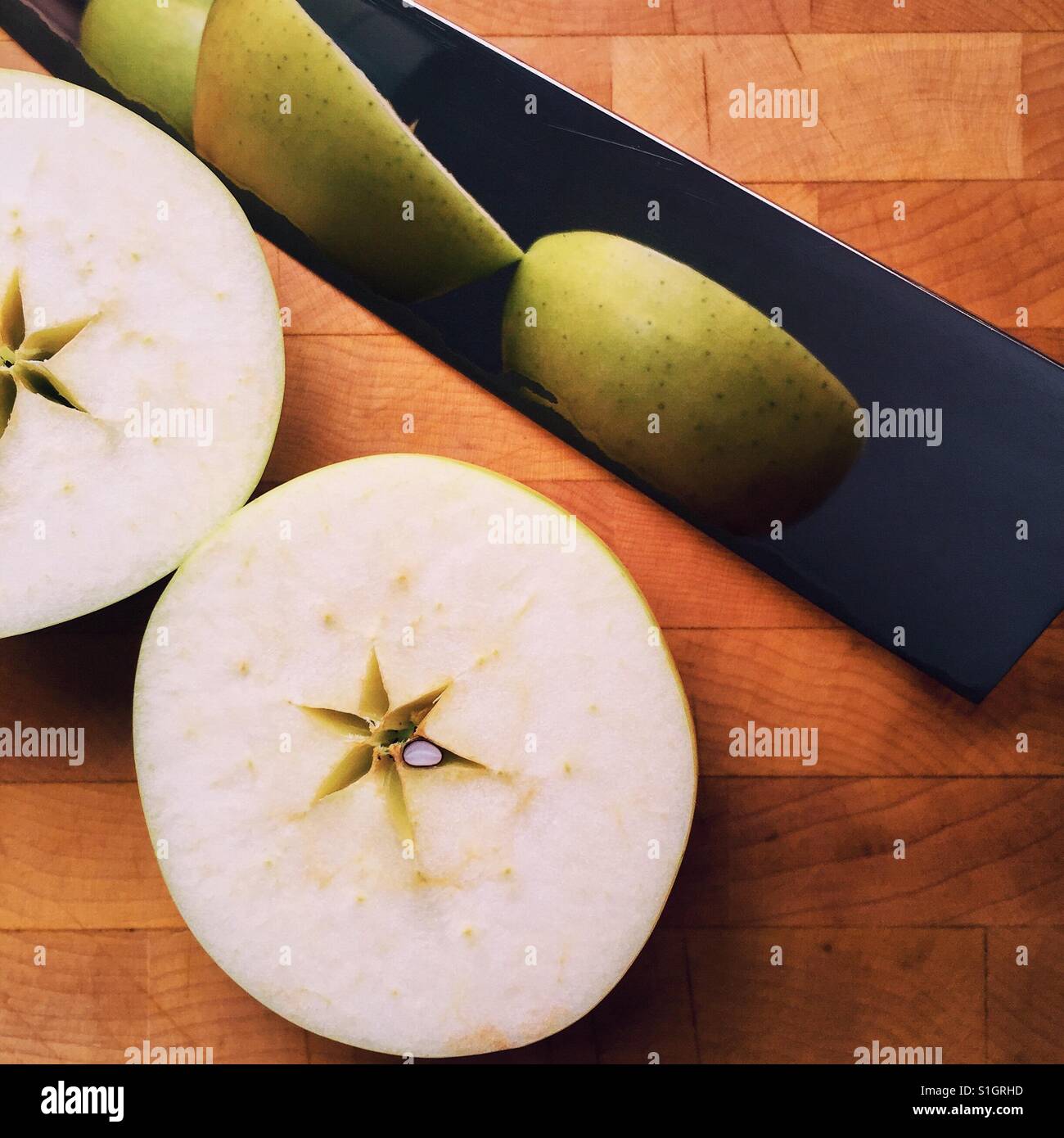 A close-up shot of an organic Orin apple cut in half resting on a cutting board with a knife Stock Photo