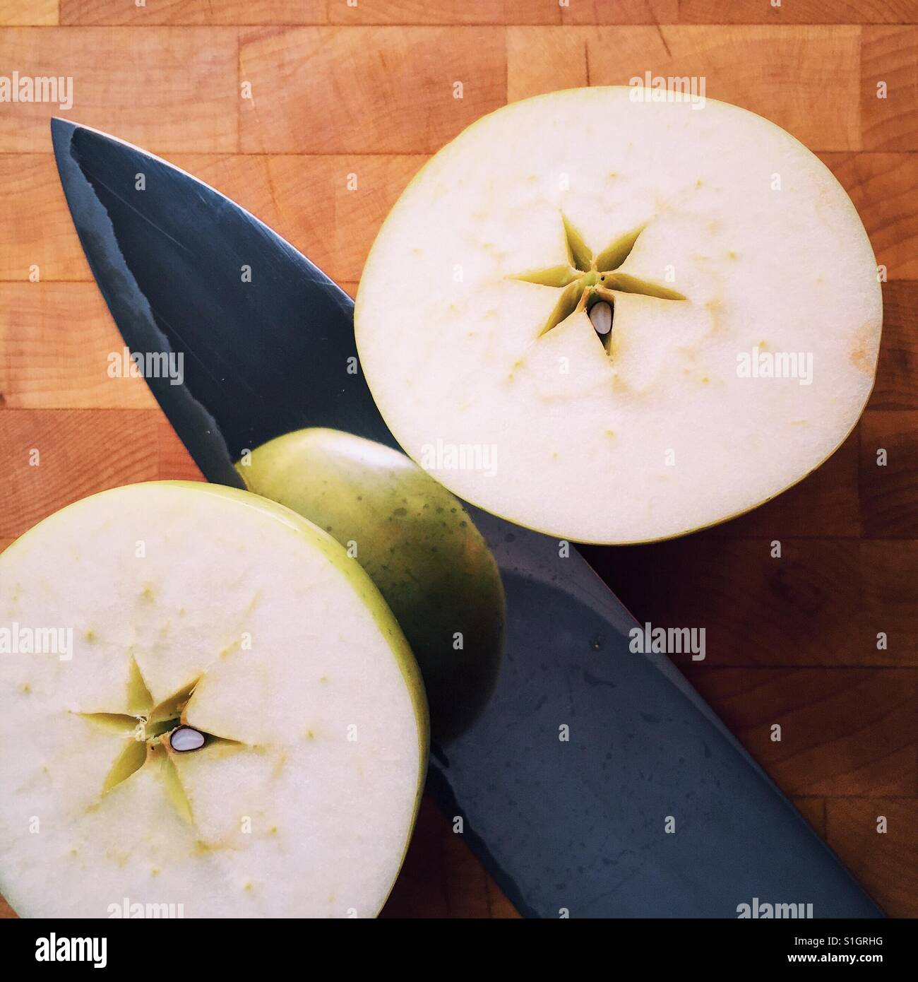 A close-up shot of an organic Orin apple cut in half resting on a cutting board with a knife Stock Photo