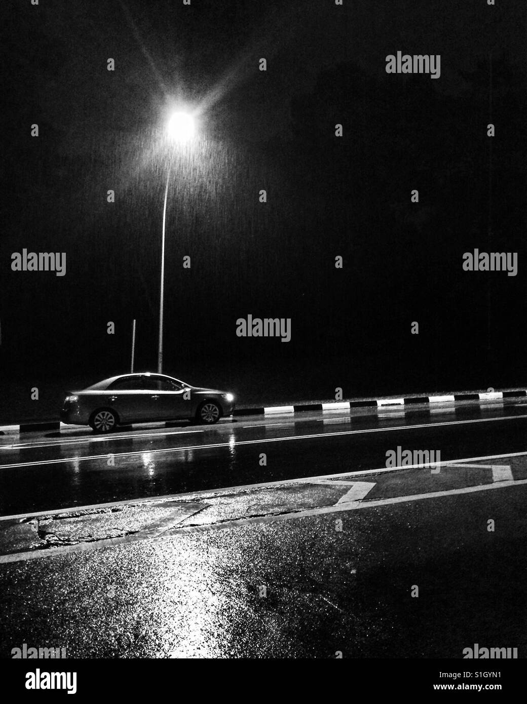 Black and white photo of a car under a street light. Stock Photo