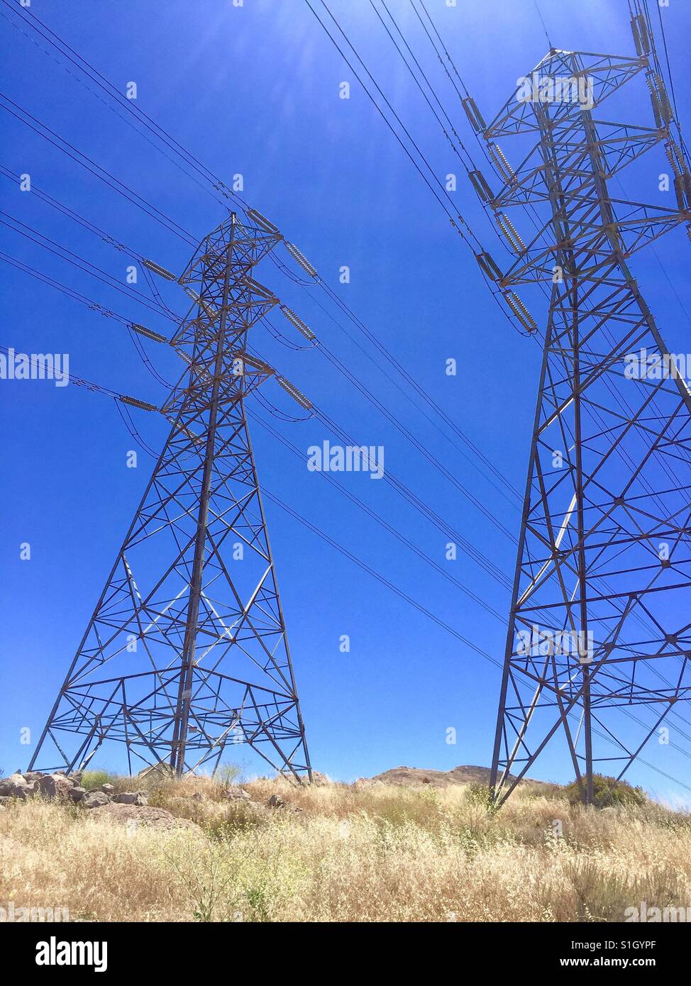 Electrical transmission towers in Southern California on top of mountain with blue sky and sun