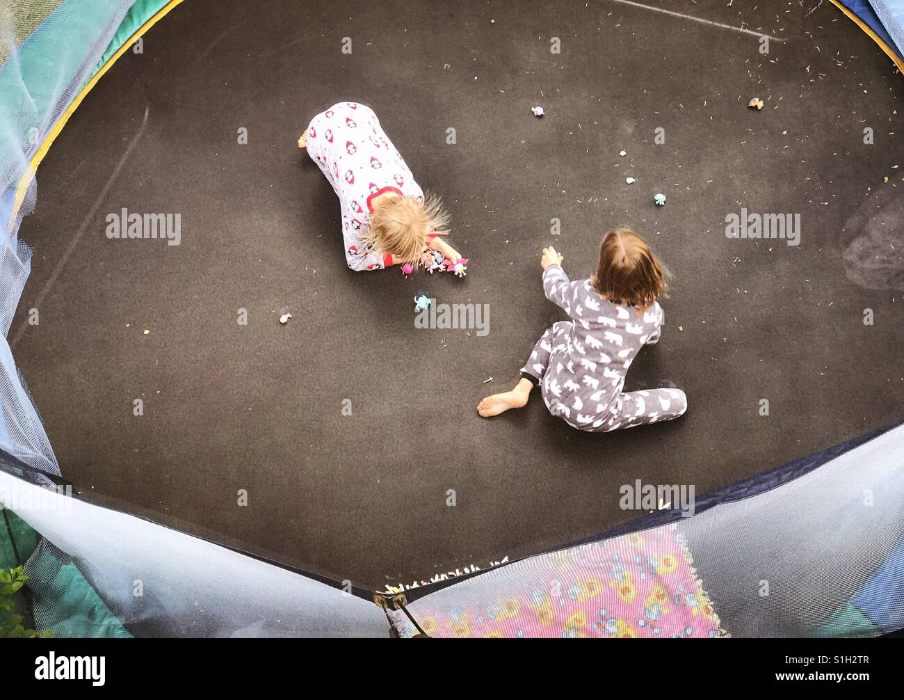 Two children are seen from overhead playing with small toys on a trampoline. - Smartphone Captured Stock Image