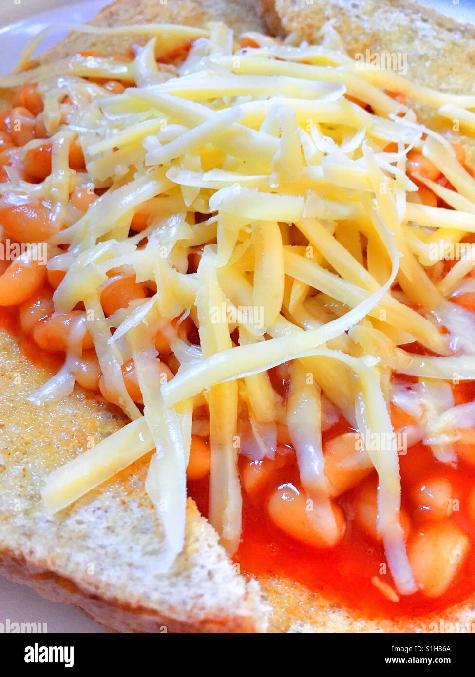 Beans on toast topped with cheddar cheese. Stock Photo