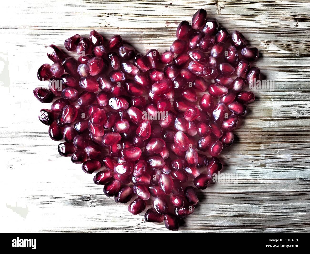 Pomegranate arils (seeds), Punica granatum in a heart shape on bamboo board - Smartphone Captured Stock Image