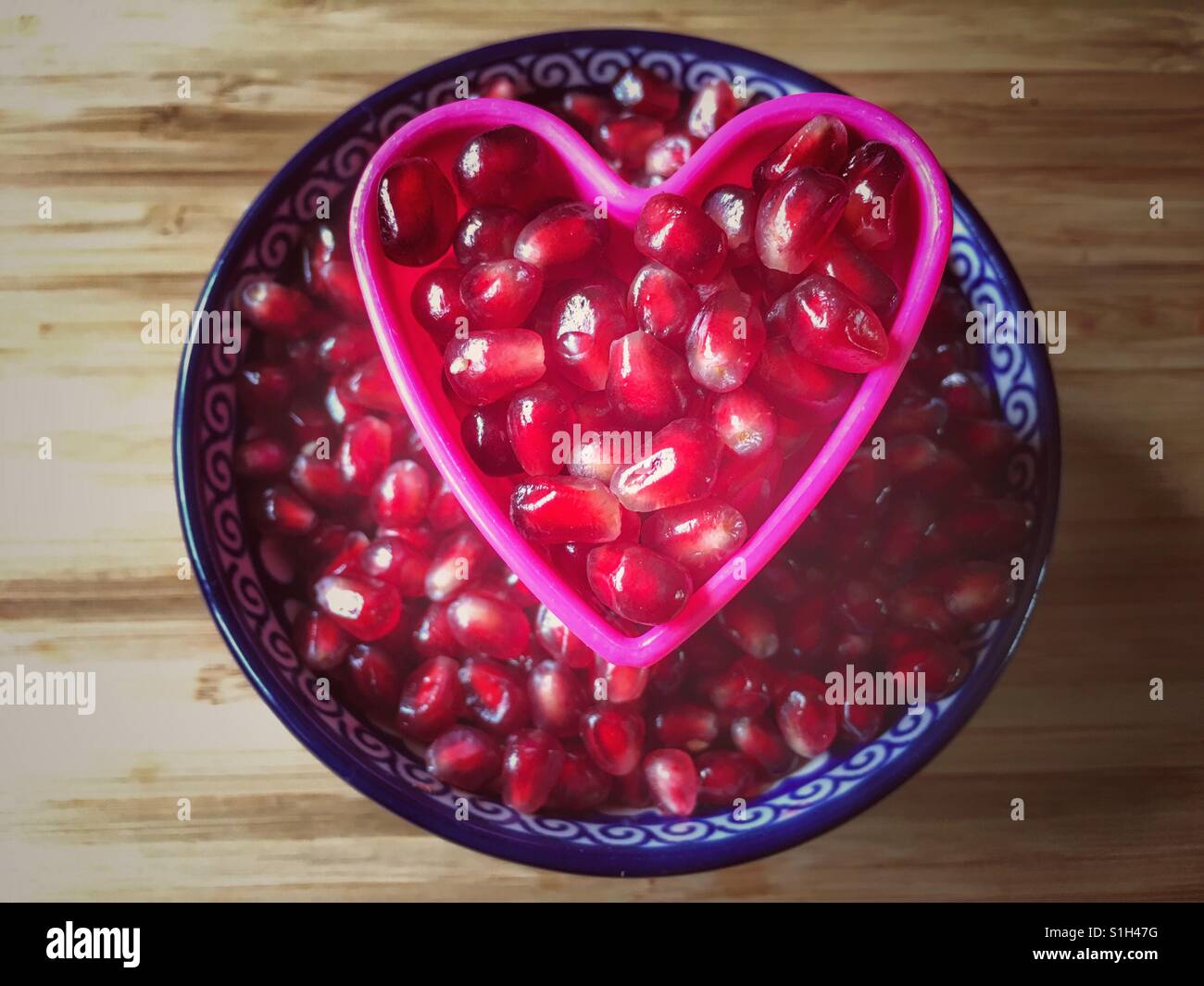A bowl of Pomegranate arils (seeds), Punica granatum with a pink heart inset - Smartphone Captured Stock Image