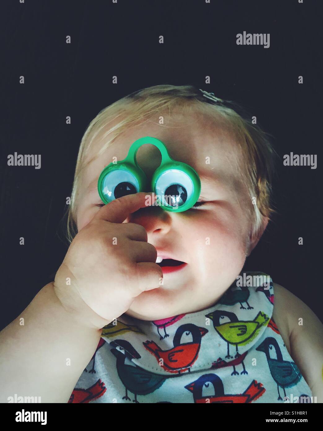 Baby girl lying down and playing with funny eyes. - Smartphone Captured Stock Image