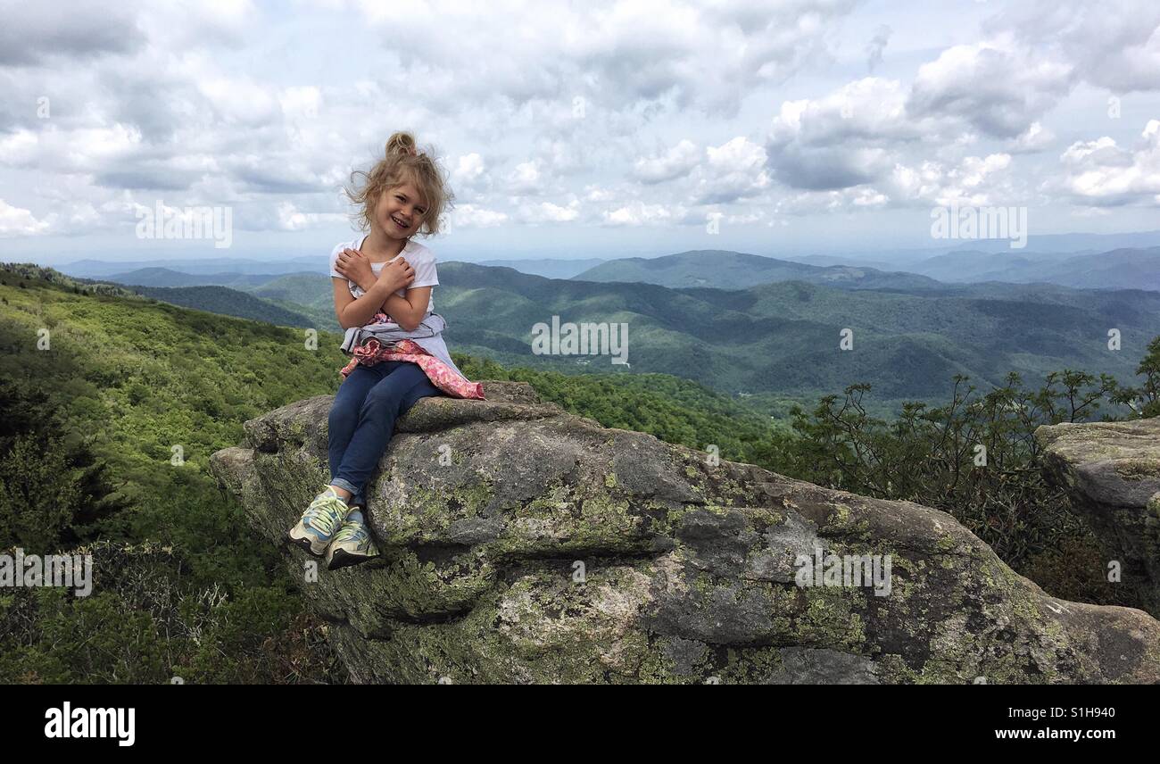 A little girl sits on a large boulder embracing her love of the mountains and outdoors. Stock Photo