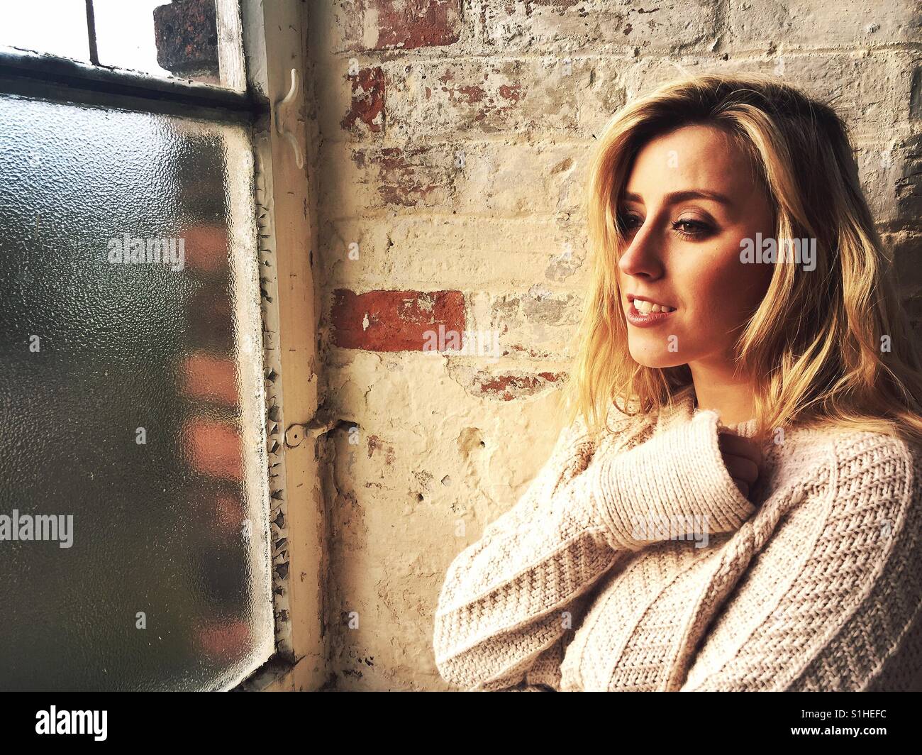 Beautiful young Caucasian blond woman looking out of the window smiling Stock Photo