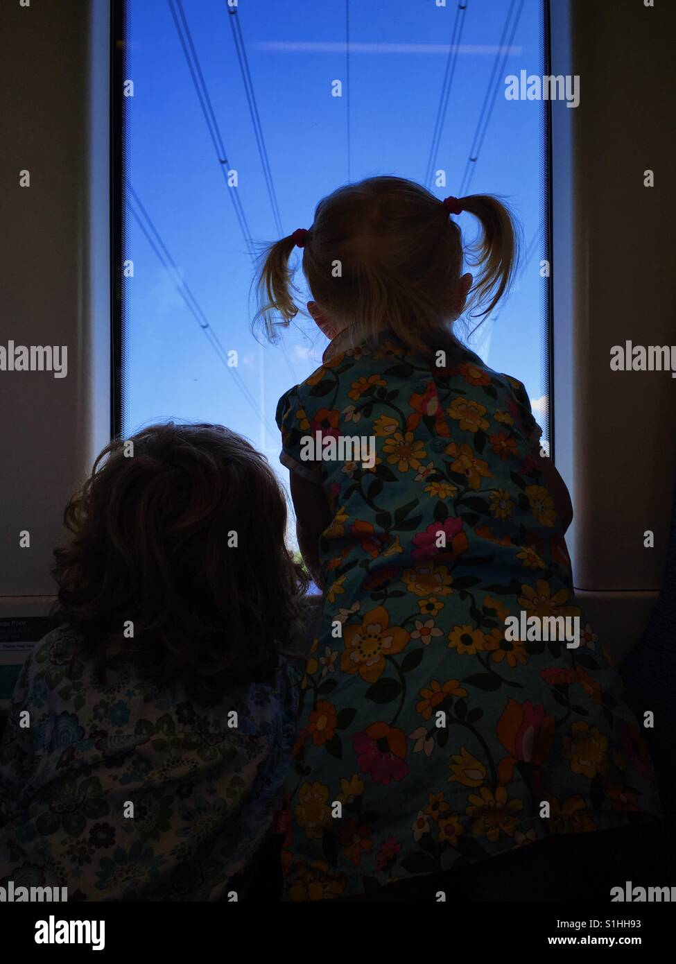 Silhouette of two children looking out train window, from behind with blue sky background. - Smartphone Captured Stock Image