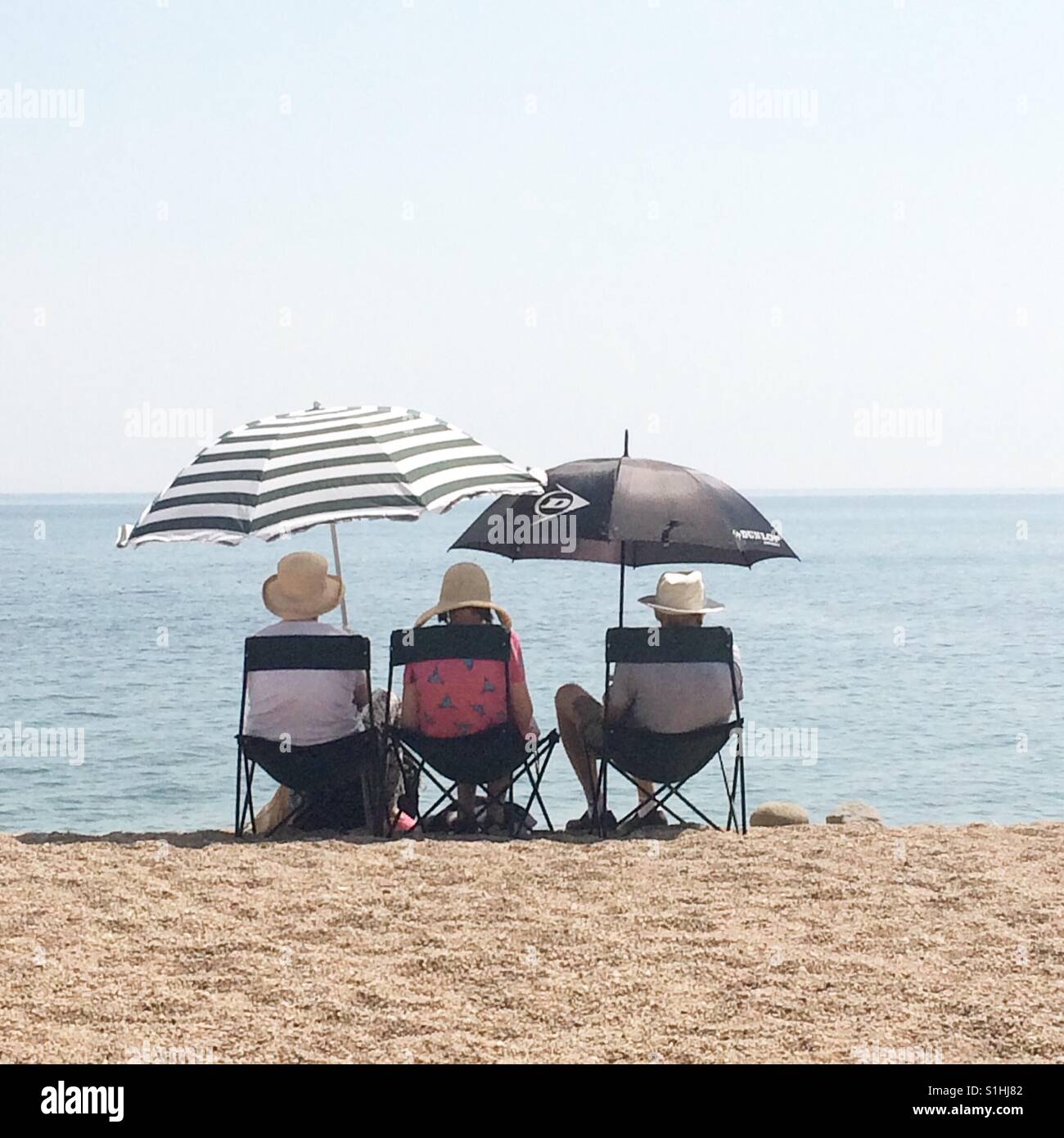 A group of elderly people sit on deck chairs under umbrellas on one of the hottest days of the year at West Bay, Dorset Stock Photo