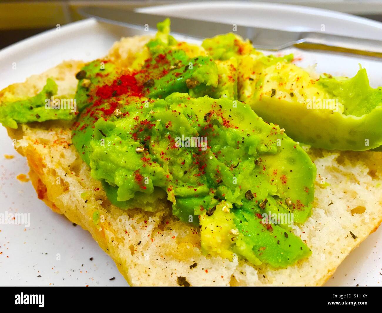 Crashed avocado on white bread roll with paprika and black pepper - Smartphone Captured Stock Image