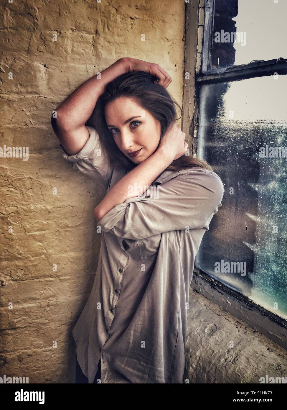 Beautiful you woman standing by the window hands touching head - Smartphone Captured Stock Image