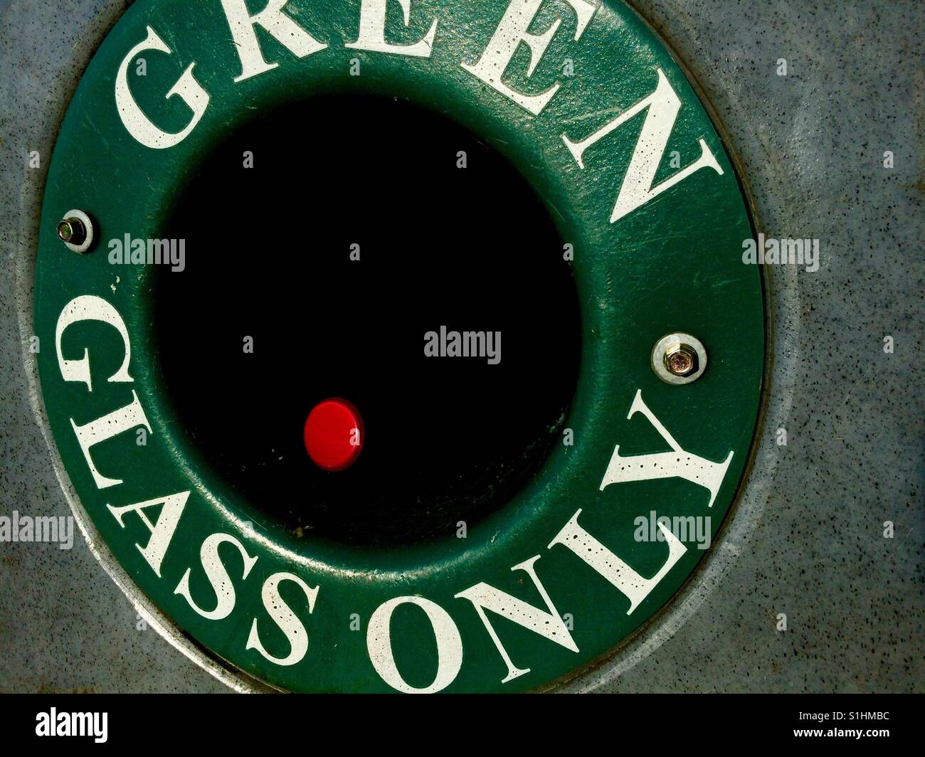A green bottle bank and a red bottle cap as a juxtaposition of complementary colours. Recycling concept. Stock Photo