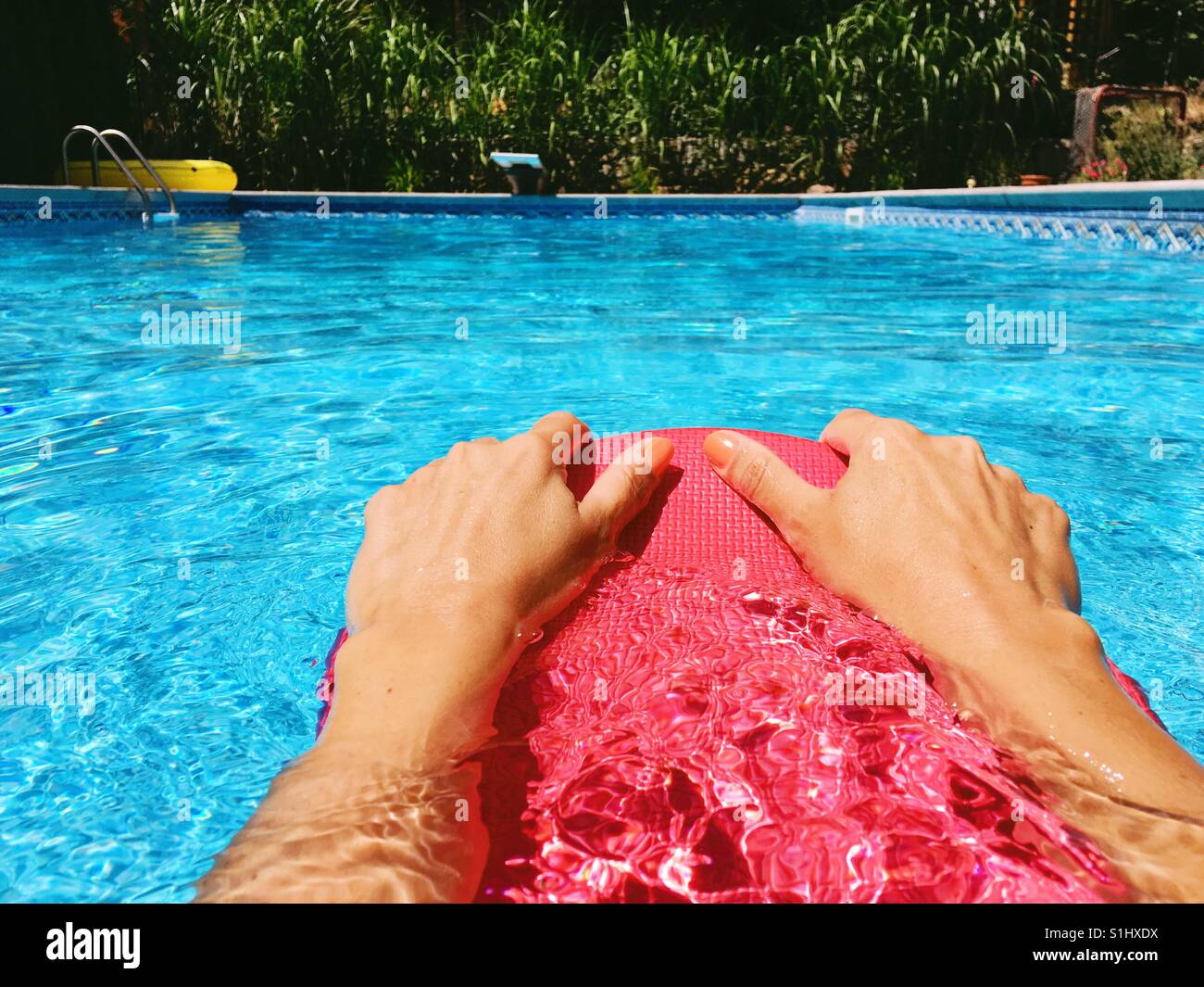 Woman's hands holding onto a kick board in an outdoor swimming pool on a sunny day. - Smartphone Captured Stock Image