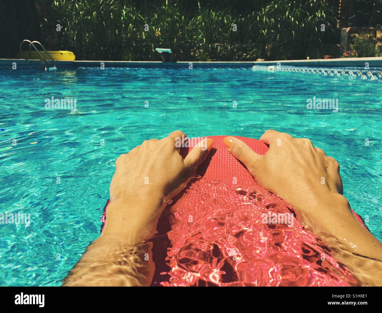Swimming in an outdoor swimming pool. Close up of woman's hands holding onto a red kick board. - Smartphone Captured Stock Image
