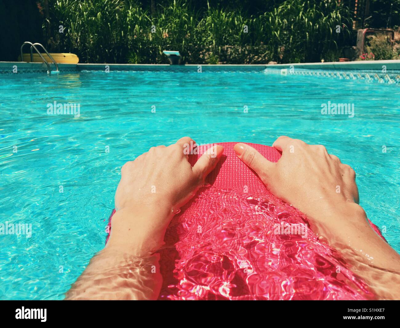 Woman swimmer holding onto a kick board while swimming in an outdoor swimming pool on a sunny day. - Smartphone Captured Stock Image