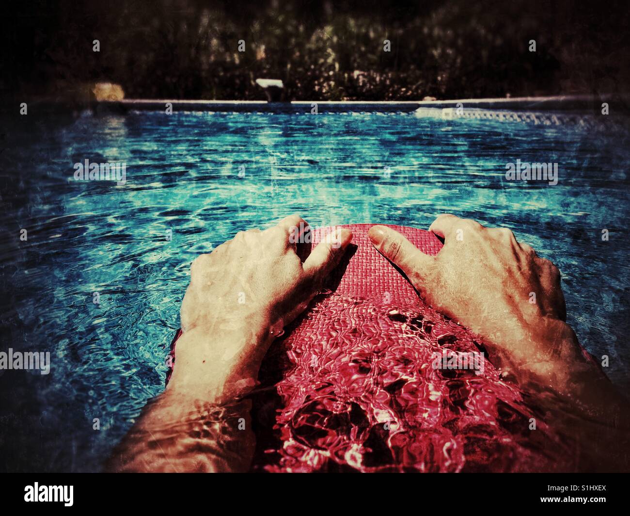 Swimmer's hands holding onto a kick board while swimming in an outdoor swimming pool. Distressed image. Stock Photo