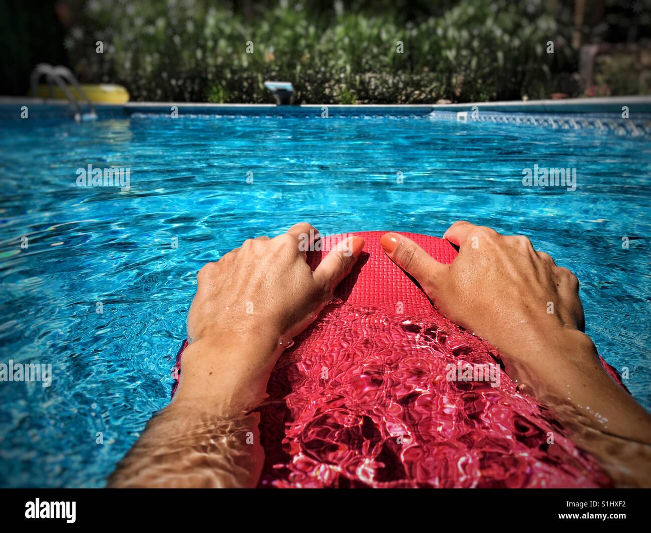 Close up of swimmer's hands holding onto a kick board in an outdoor swimming pool on a sunny day. - Smartphone Captured Stock Image