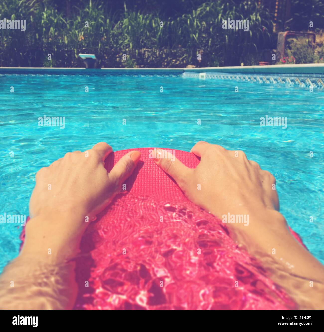 Close up of swimmer's hands holding onto a kick board while swimming in an outdoor swimming pool on a sunny bright day. Square crop. Stock Photo