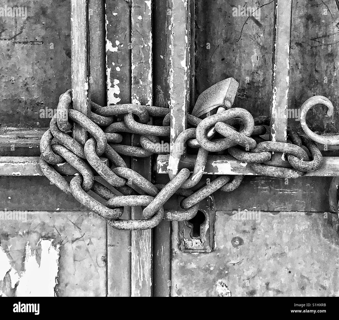 A photo in black and white of a weathered door securely locked with an equally weathered lock and chain - Smartphone Captured Stock Image