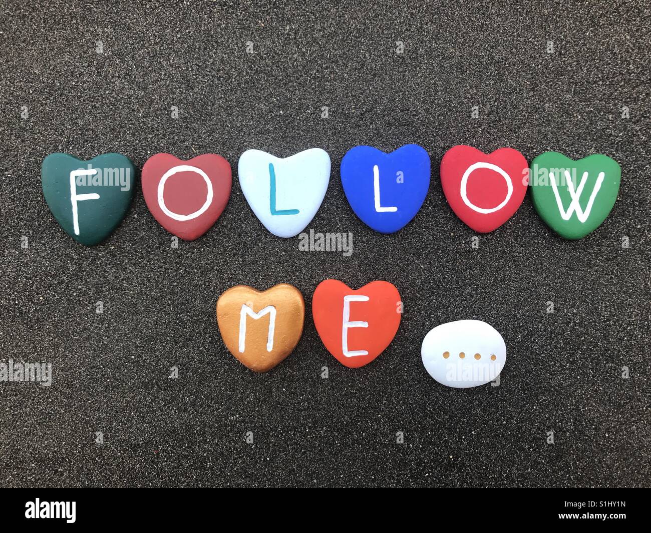 Follow me sentence with multicolored stone hearts over black volcanic sand - Smartphone Captured Stock Image