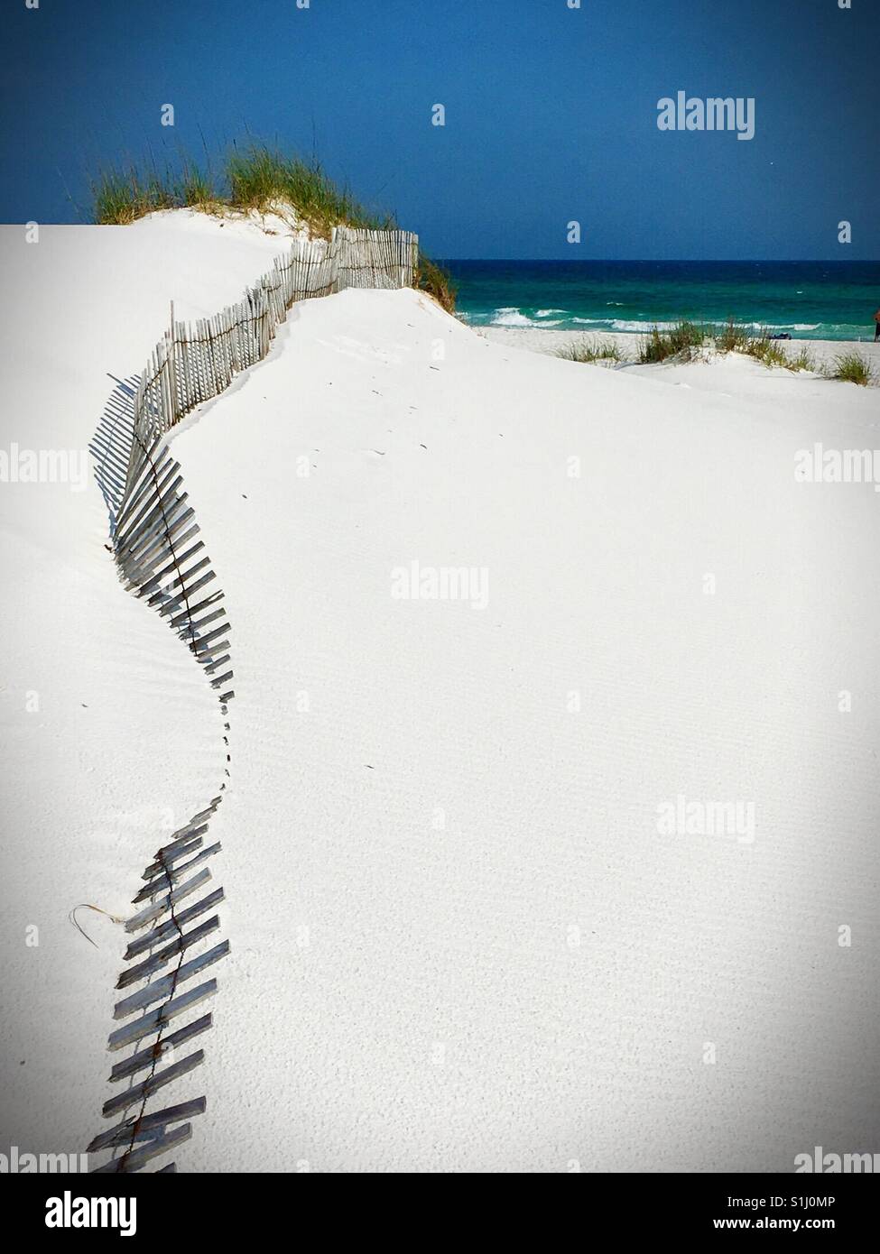 A small wooden fence in the white sand extends out to the blue green ocean water - Smartphone Captured Stock Image