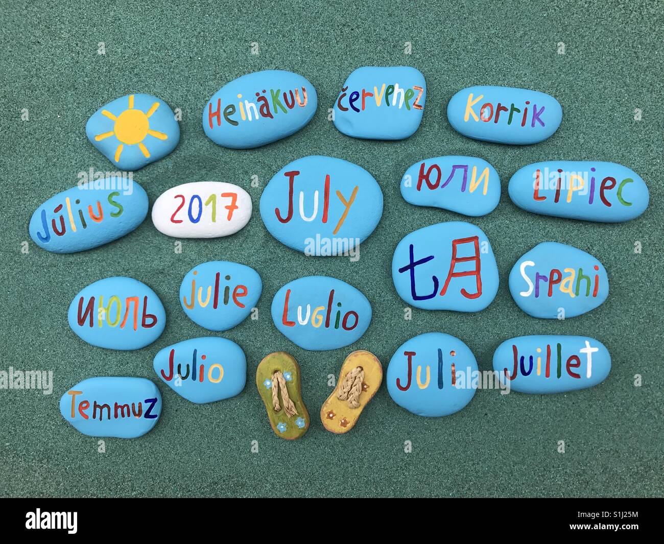 July 2017 in many languages on colored stones over green sand - Smartphone Captured Stock Image