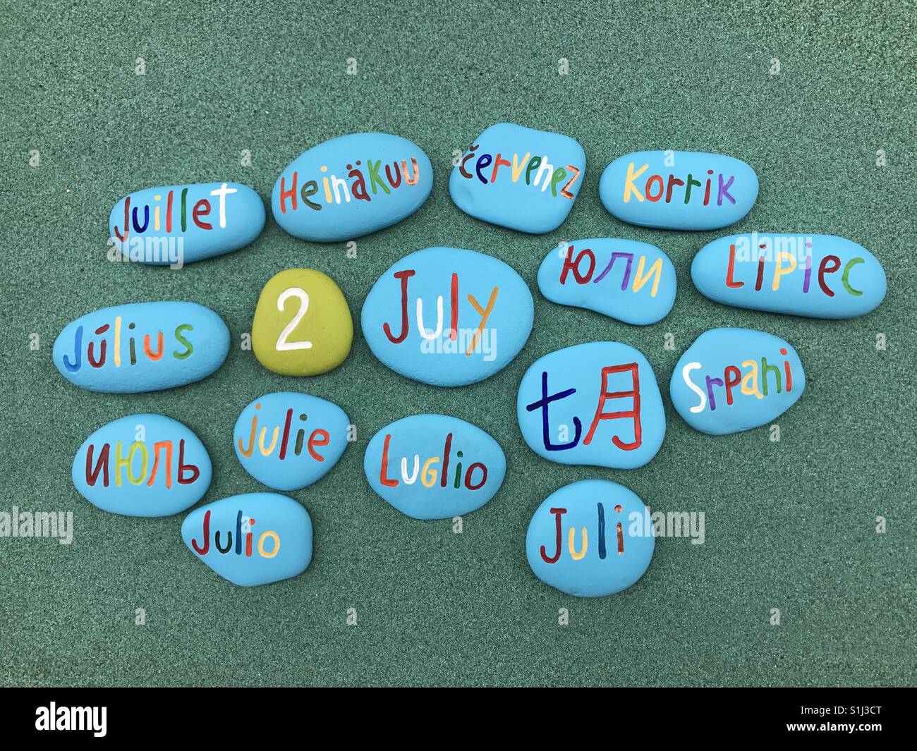 2 July, calendar date with colored stones in many languages over green sand - Smartphone Captured Stock Image