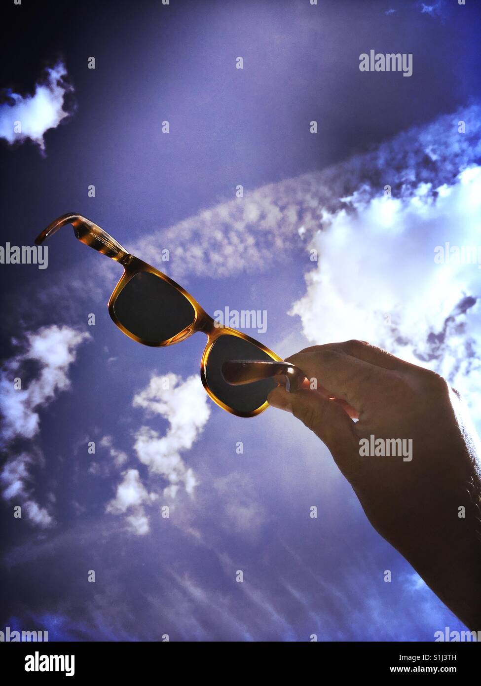 Man holding sunglasses agains blue sky - Smartphone Captured Stock Image