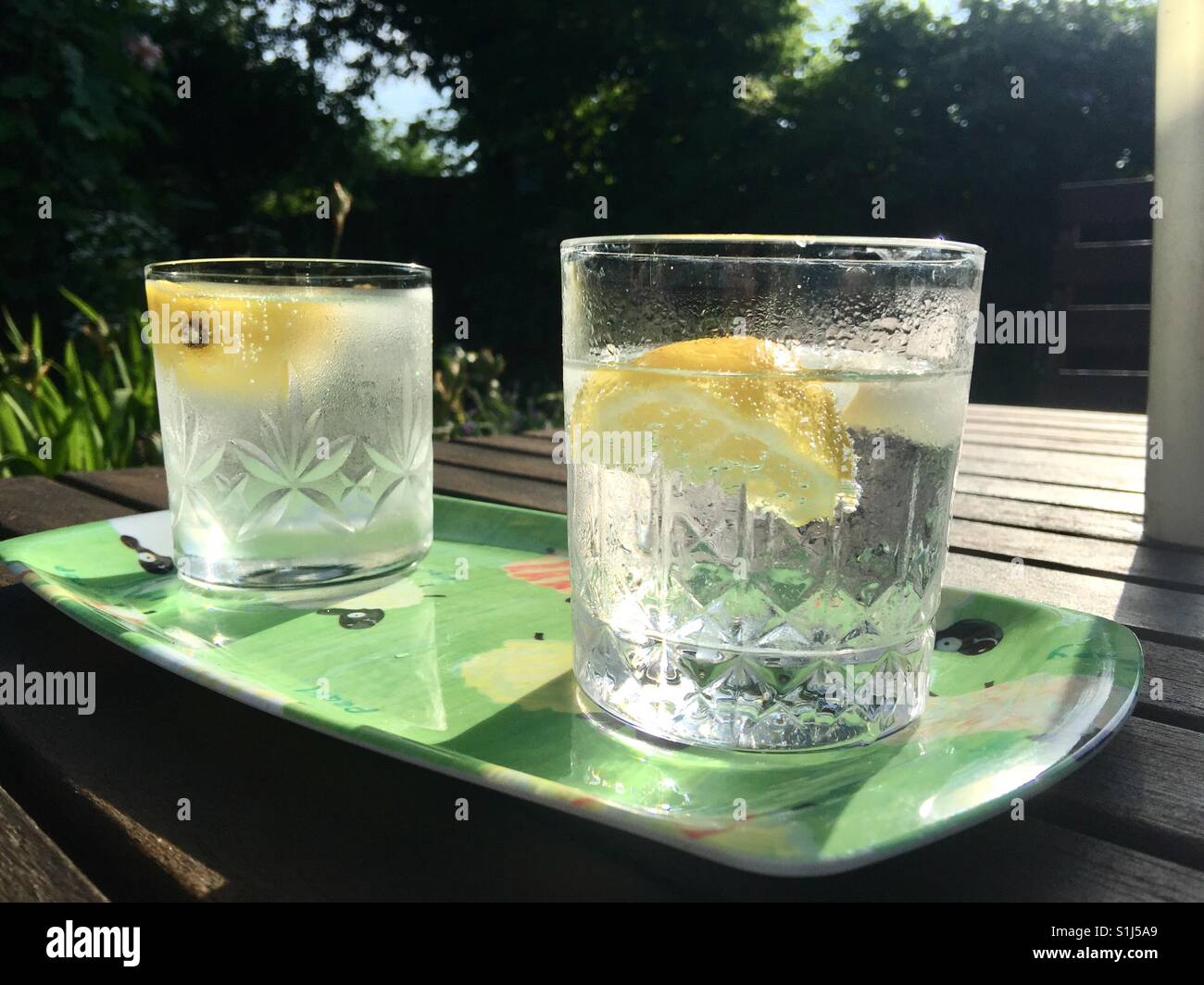 Two glasses of gin and tonic on a tray sitting on a garden table  with strong sunshine in the background. Stock Photo