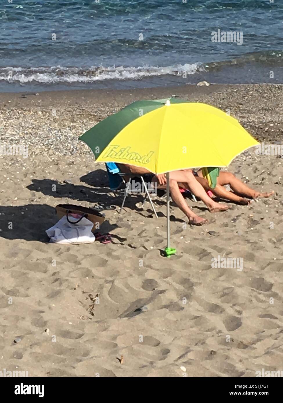 Two people hidden behind a yellow parasol on a sunny beach Stock Photo -  Alamy