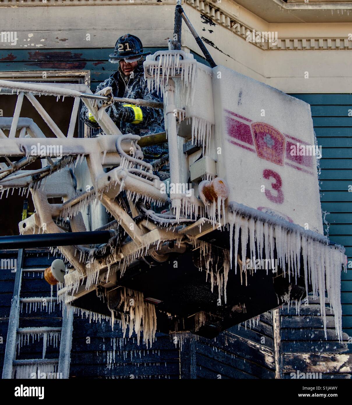 Firefighter fights with ice and frigid temperatures to dismantle hose couplings at the scene of an apartment house fire Stock Photo