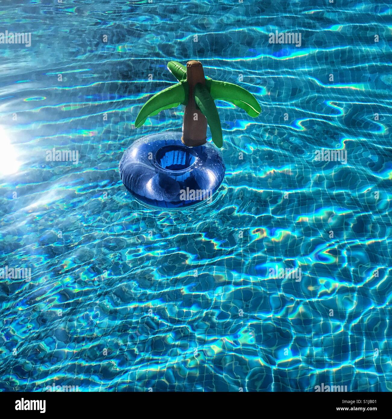 Inflatable palm tree island floating in sunny blue swimming pool Stock Photo