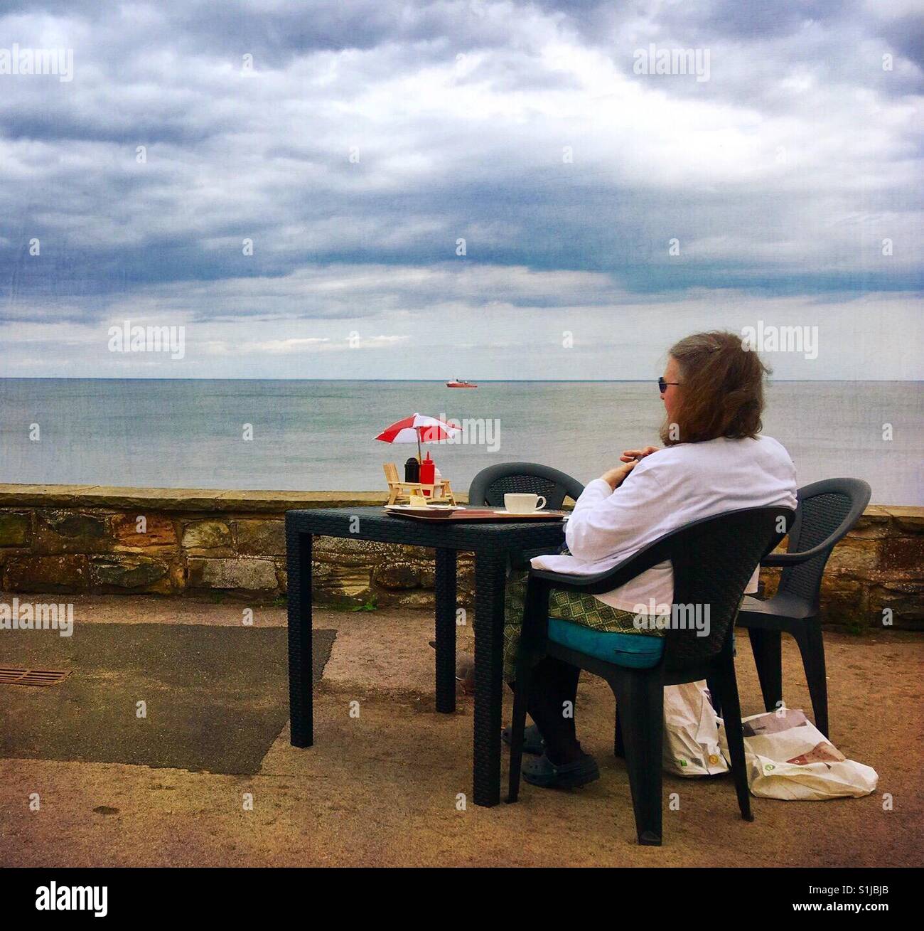 Woman having a coffee by the sea - Smartphone Captured Stock Image