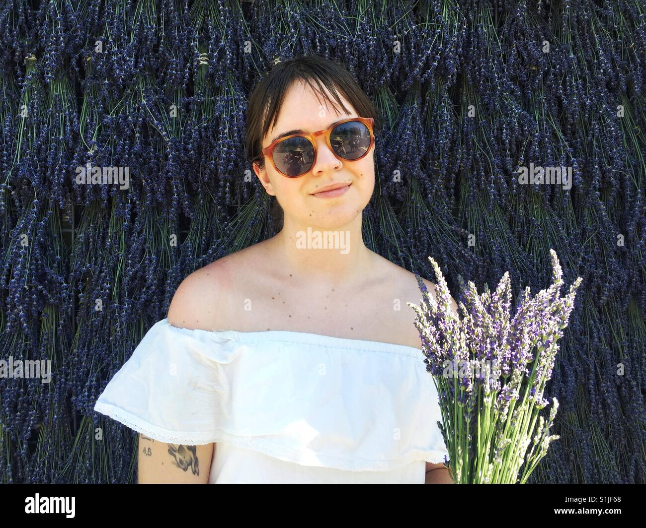 Young female in white dress snd sunglasses posing in front of wall of lavender Stock Photo