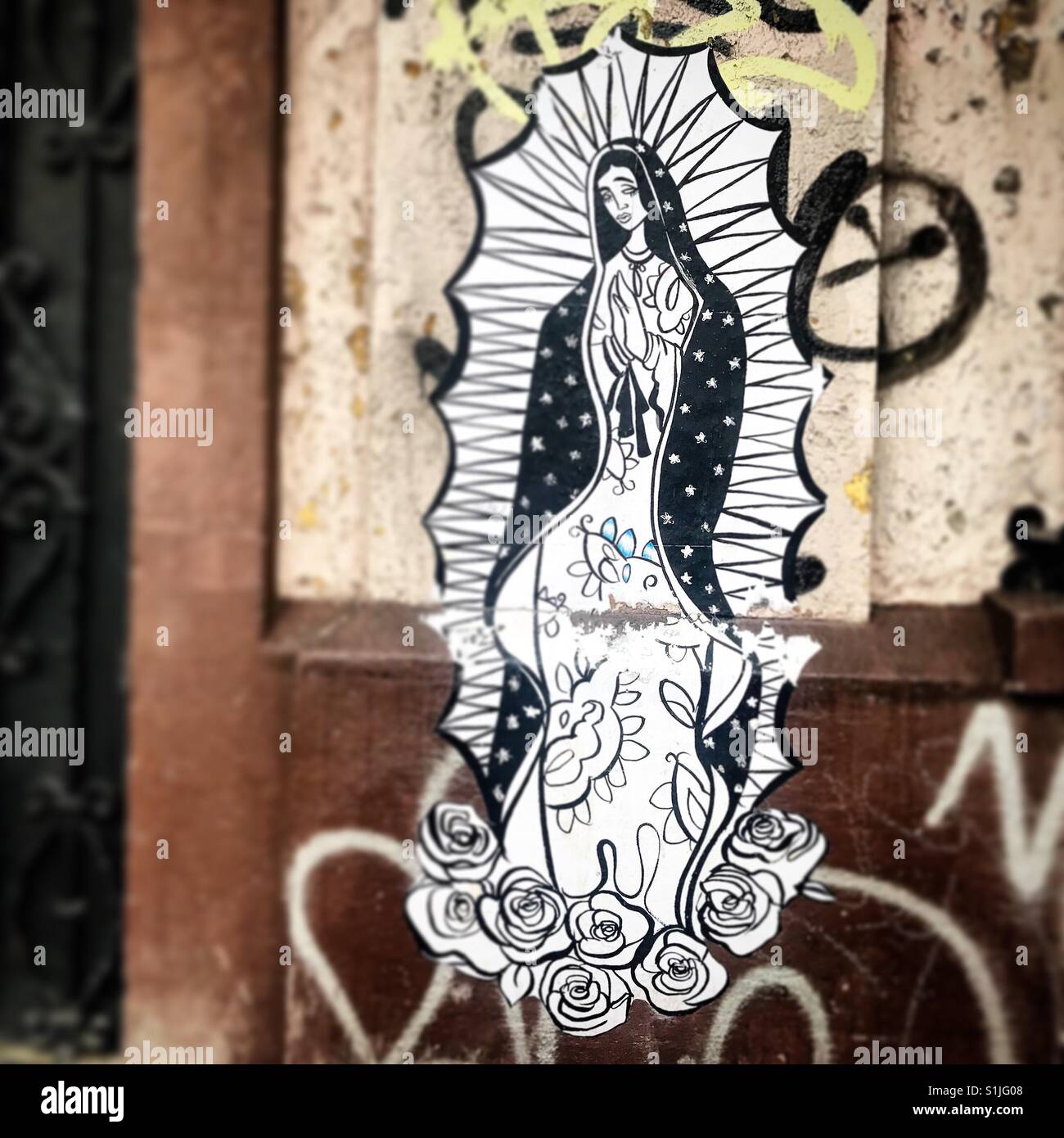 A paper sticker with the image of Our Lady of Guadalupe surrounded by graffiti in a street of Mexico City, Mexico Stock Photo
