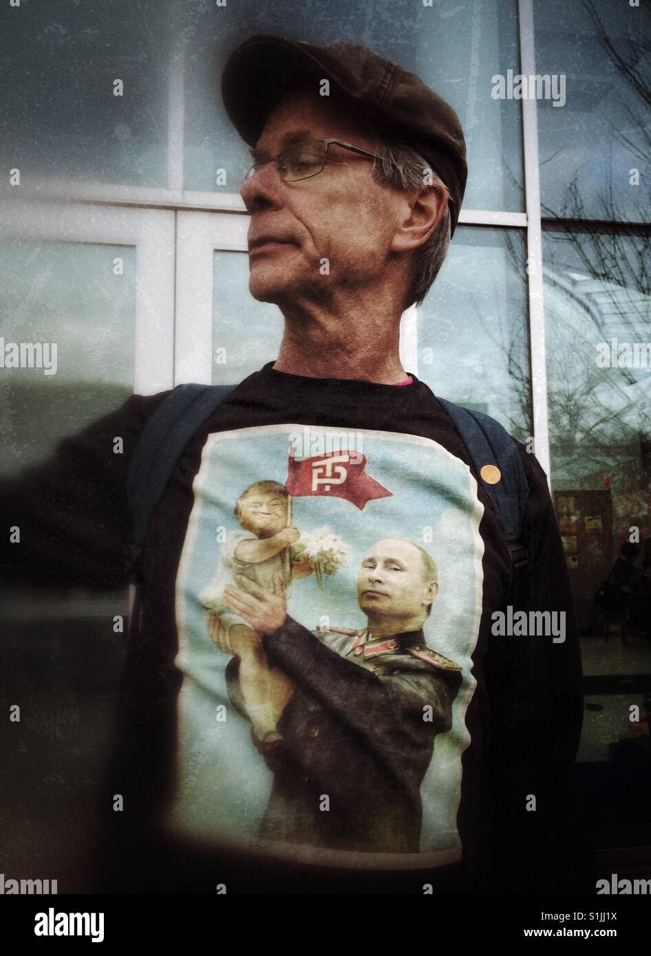 Middle age Caucasian male wearing a cap and a shirt with caricature of Putin holding baby Trump in his hands - Smartphone Captured Stock Image