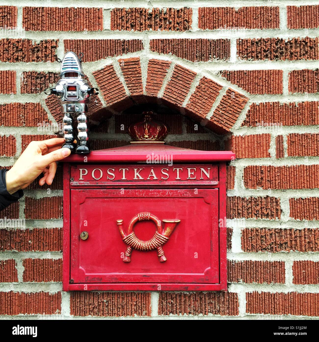 Red vintage letterbox with word Postkasten and horn inside brick wall with Robot toy standing on it - Smartphone Captured Stock Image