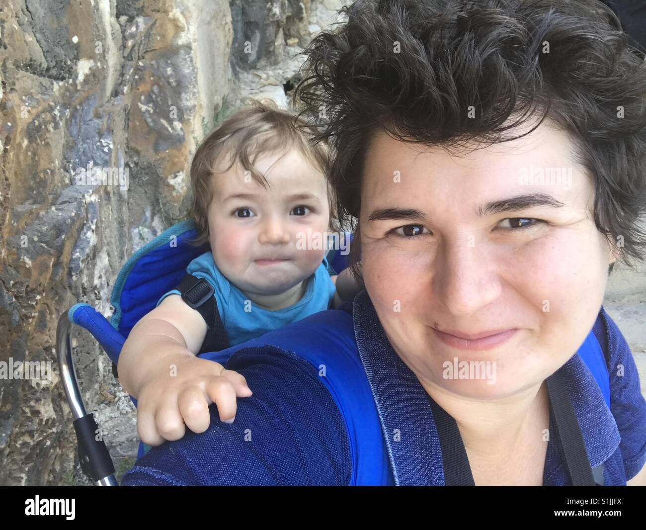 Cheerful woman carrying his son in carrier - Smartphone Captured Stock Image