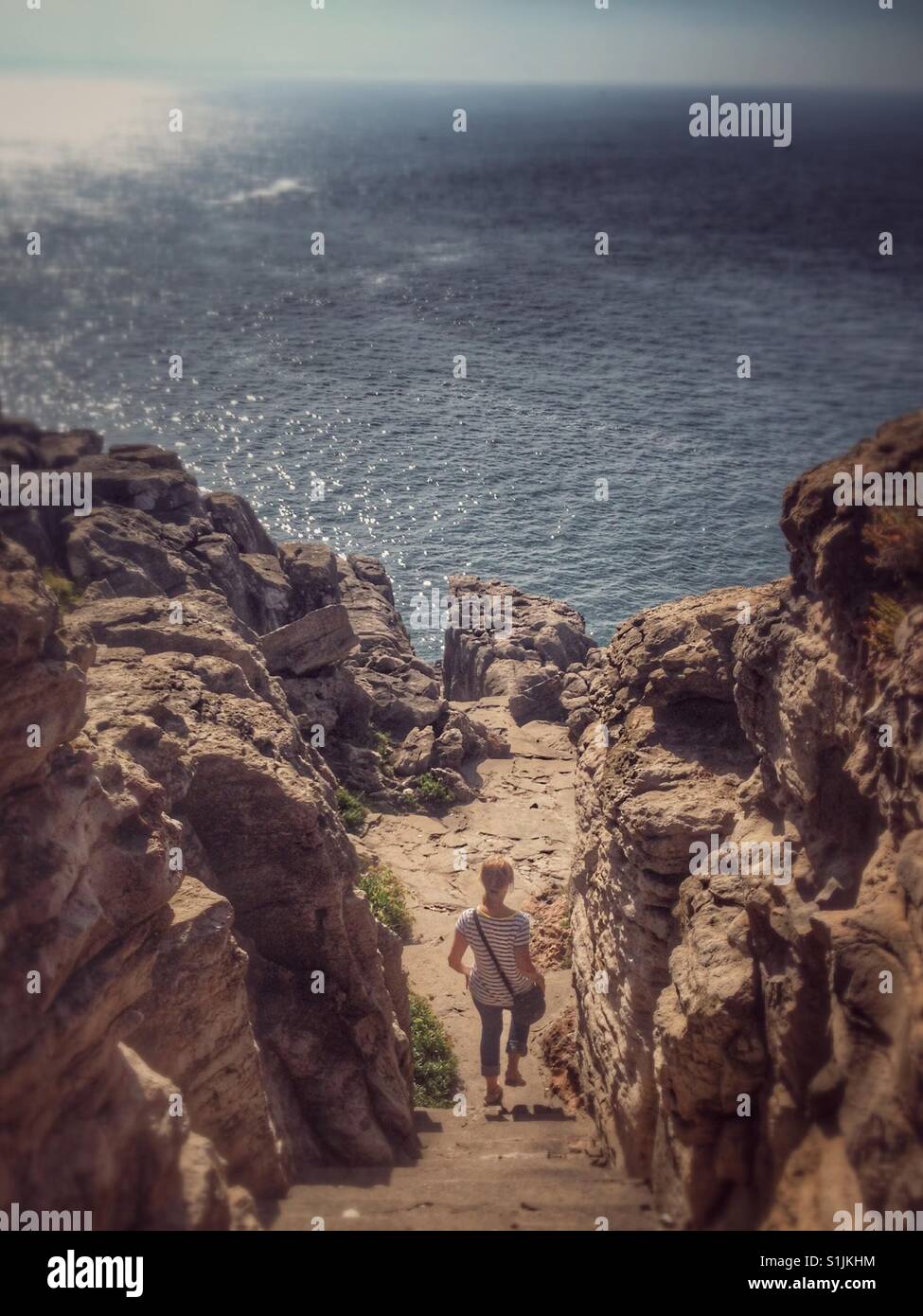Woman walking down stairs in front of Ocean view from cliffs in Peniche, Portugal . Stock Photo