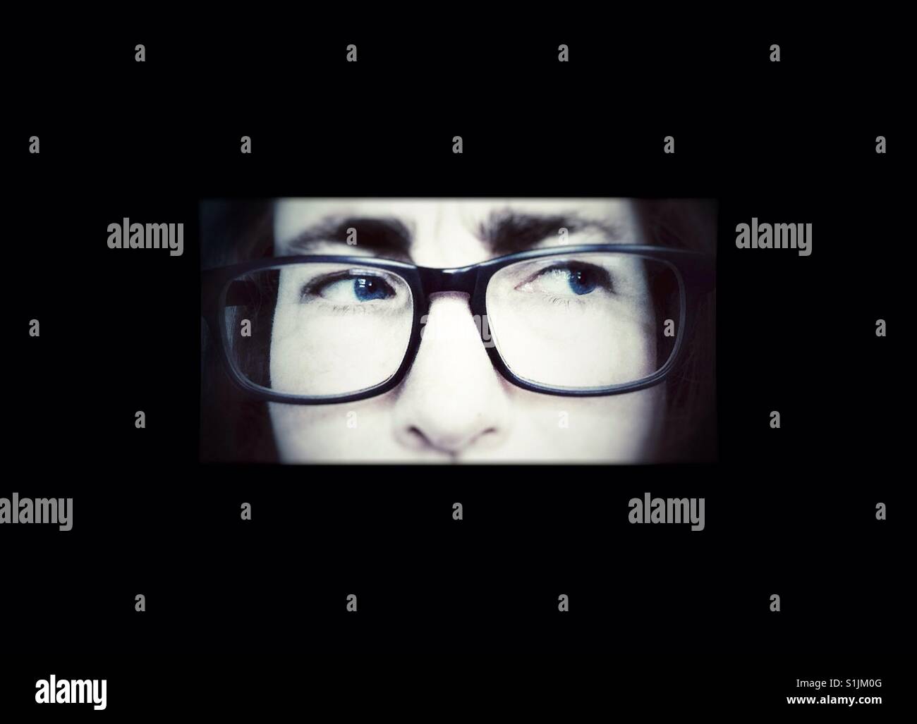 A pensive woman wearing glasses peers out of the darkness - Smartphone Captured Stock Image