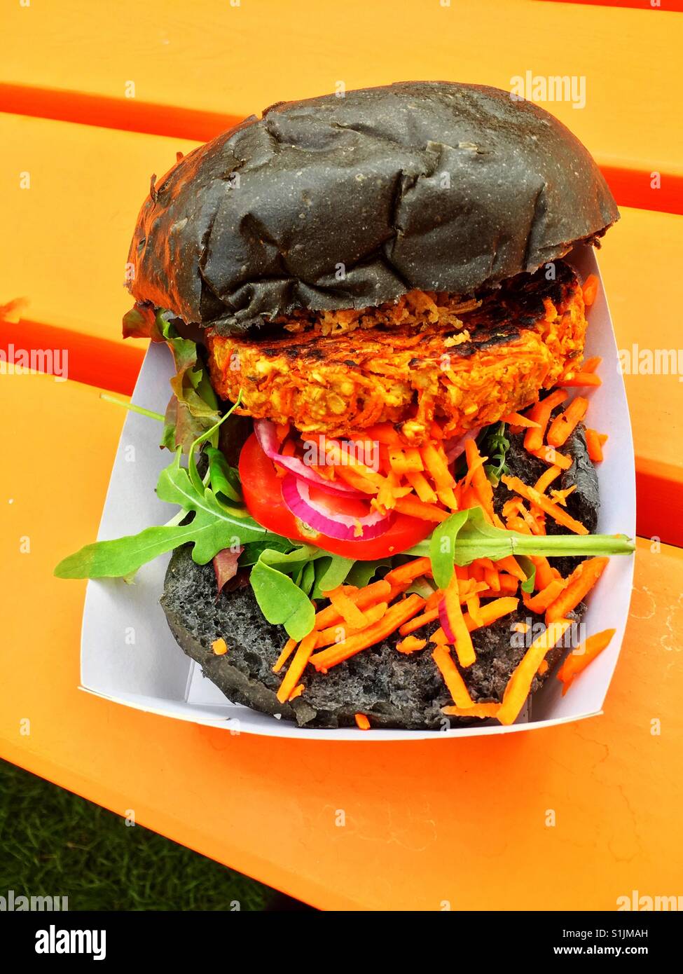 Eating an orange vegetarian carrot burger on a bright orange picnic table Stock Photo