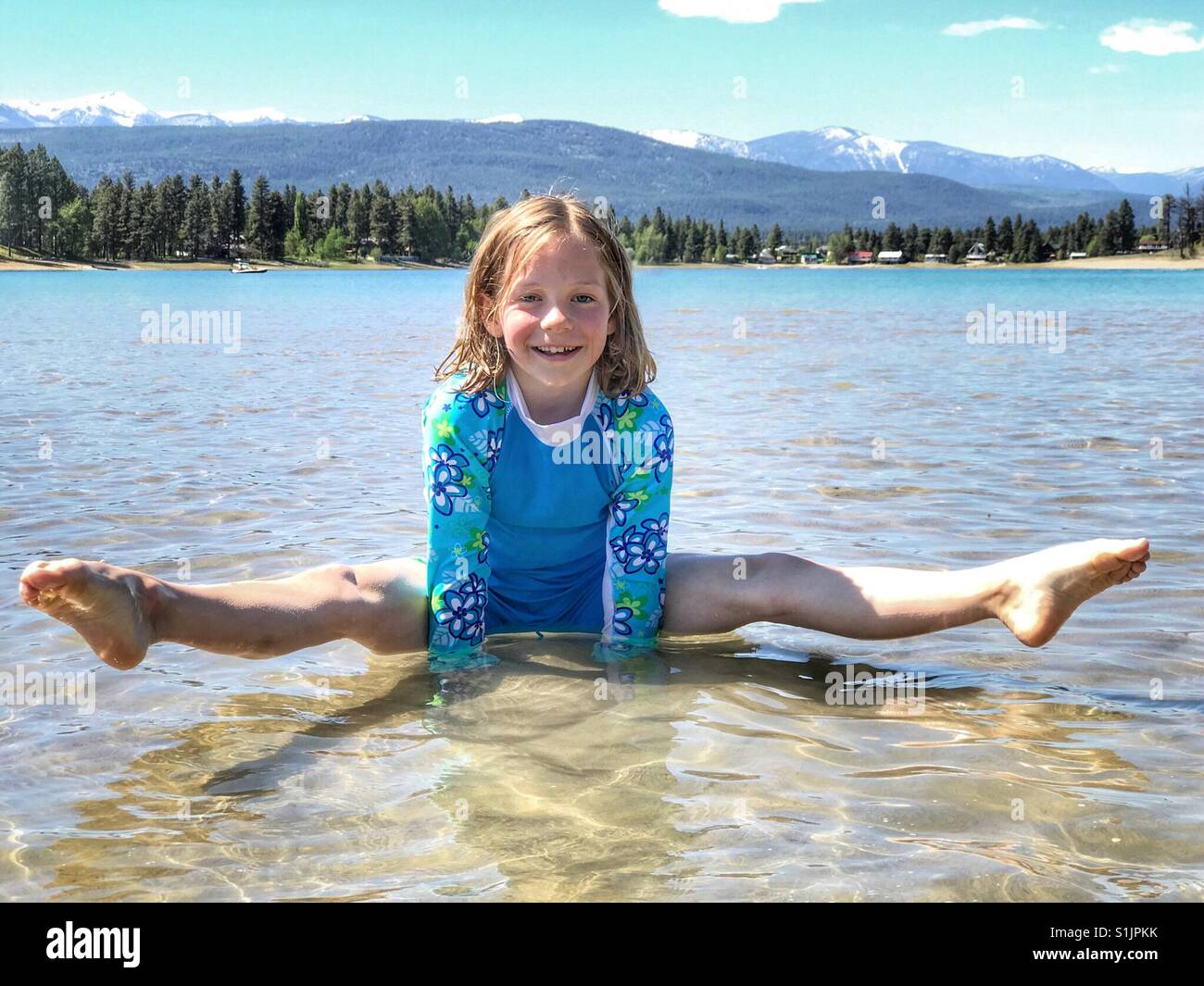 A girl balances on her hands in the shallows of a small lake. - Smartphone Captured Stock Image